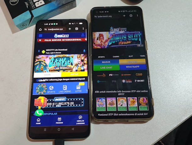 Two smartphones are displayed on a white surface, both showing gambling websites with colorful graphics, text, and various options for logging in and accessing games. The screens are bright and filled with promotional content related to casino and slot games.